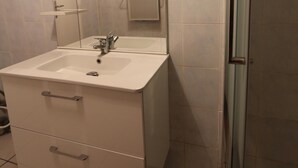 Ein Badezimmer mit weißem Waschbecken, Spiegel und einer Duschkabine aus Glas.