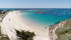 A coastal beach with a sandy shoreline, clear turquoise waters, and rocky outcrops.