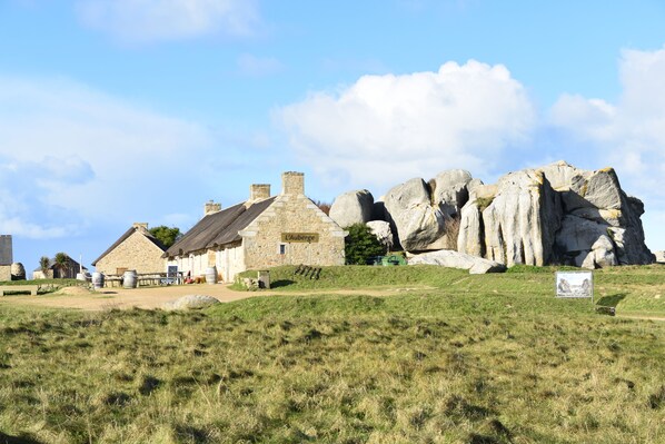 Un edificio de piedra con techo de paja, un letrero que dice 'L'Auberge' y una gran formación rocosa al fondo.