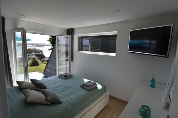 A bedroom with a bed, a TV, a window, and a view of the outdoors.