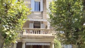 Un bâtiment doté d’un balcon, d’une enseigne et d’arbres au premier plan.