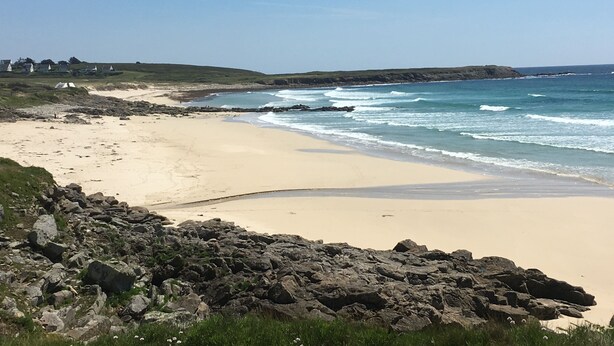 Une plage avec un premier plan rocheux, une rive sablonneuse et des vagues déferlantes.