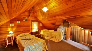 Ein gemütliches Schlafzimmer im Dachgeschoss mit Holzwänden und geneigten Decken, mit zwei Betten mit Blumenmuster und einem kleinen Tisch mit einer Lampe.