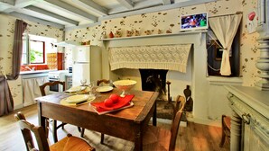 Ein Esszimmer mit Holztisch, gedeckt für vier Personen, Kamin und einer Küche im Hintergrund.