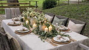 An outdoor dining area with a table set for six, surrounded by wicker chairs, under string lights.