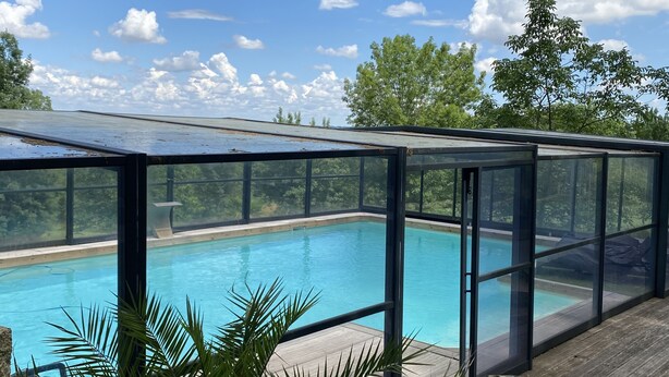 A swimming pool with a glass enclosure, surrounded by wooden decking and potted plants.