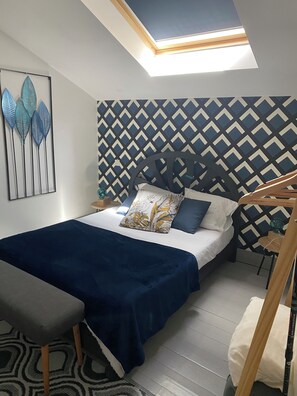 Un dormitorio con cama, escritorio, silla, pared con diseño y tragaluz.