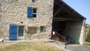 A stone building with a covered porch, a small window, and a door with blue shutters.