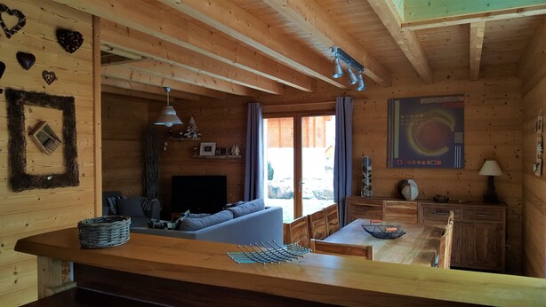 Ein gemütliches Blockhaus-Interieur mit Holzbalkendecke, einer Couch, einem Esstisch und einem Fernseher.