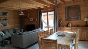 Ein gemütliches Blockhaus-Interieur mit Sofa, Esstisch, Stühlen, Holzausbau und einem großen Fenster.