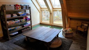 Ein gemütliches Zimmer mit Holztisch, einer Bücherwand voller Gesellschaftsspiele und einem großen Fenster mit Blick auf Bäume.
