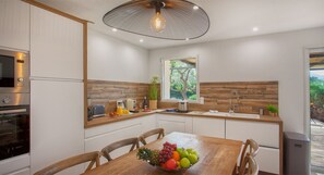 Una cocina moderna con detalles de madera, una mesa de comedor con fruta y vistas al exterior.