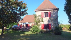 A two-story house with a red-tiled roof, a chimney, and a small garden area with a tree and a car parked nearby. - Perigordian style property (Saint-Pierre-d'Eyraud)