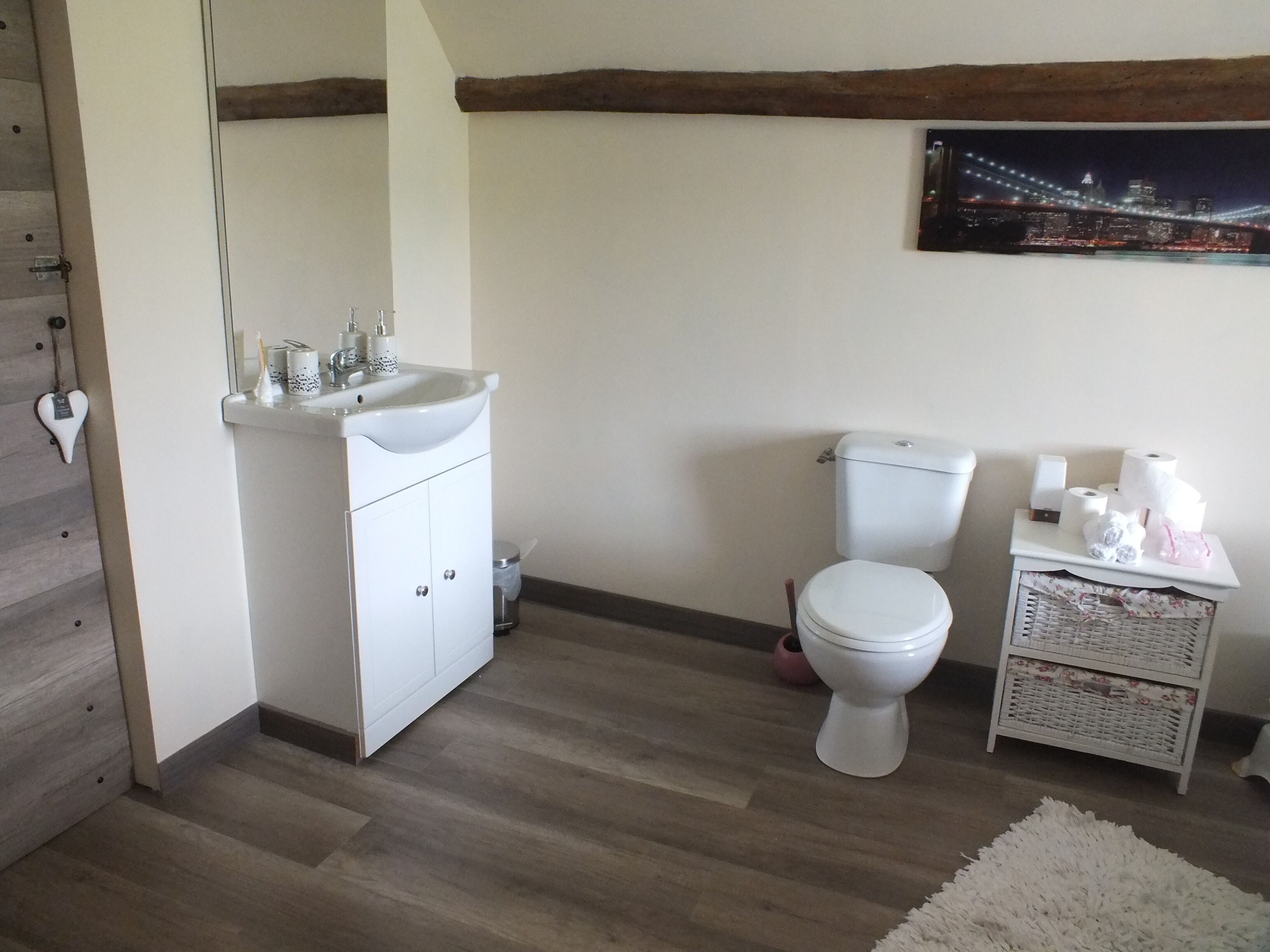 A bathroom with a white sink, toilet, and a small bedside table with toiletries.