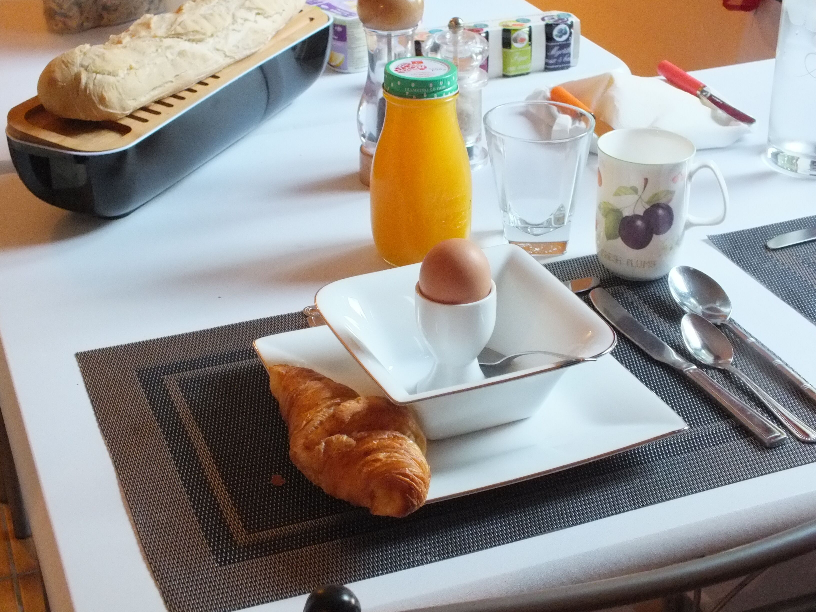 A breakfast setting with croissants, a bottle of orange juice, a cup of coffee, and a plate with an egg.