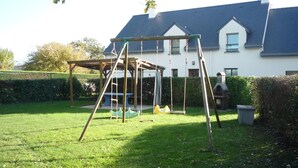 A wooden swing set in a grassy backyard with a house in the background.