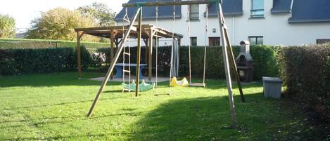 A wooden swing set in a grassy backyard with a house in the background.