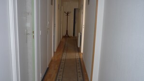 A narrow hallway with a patterned carpet, white walls, and a coat rack in the center.