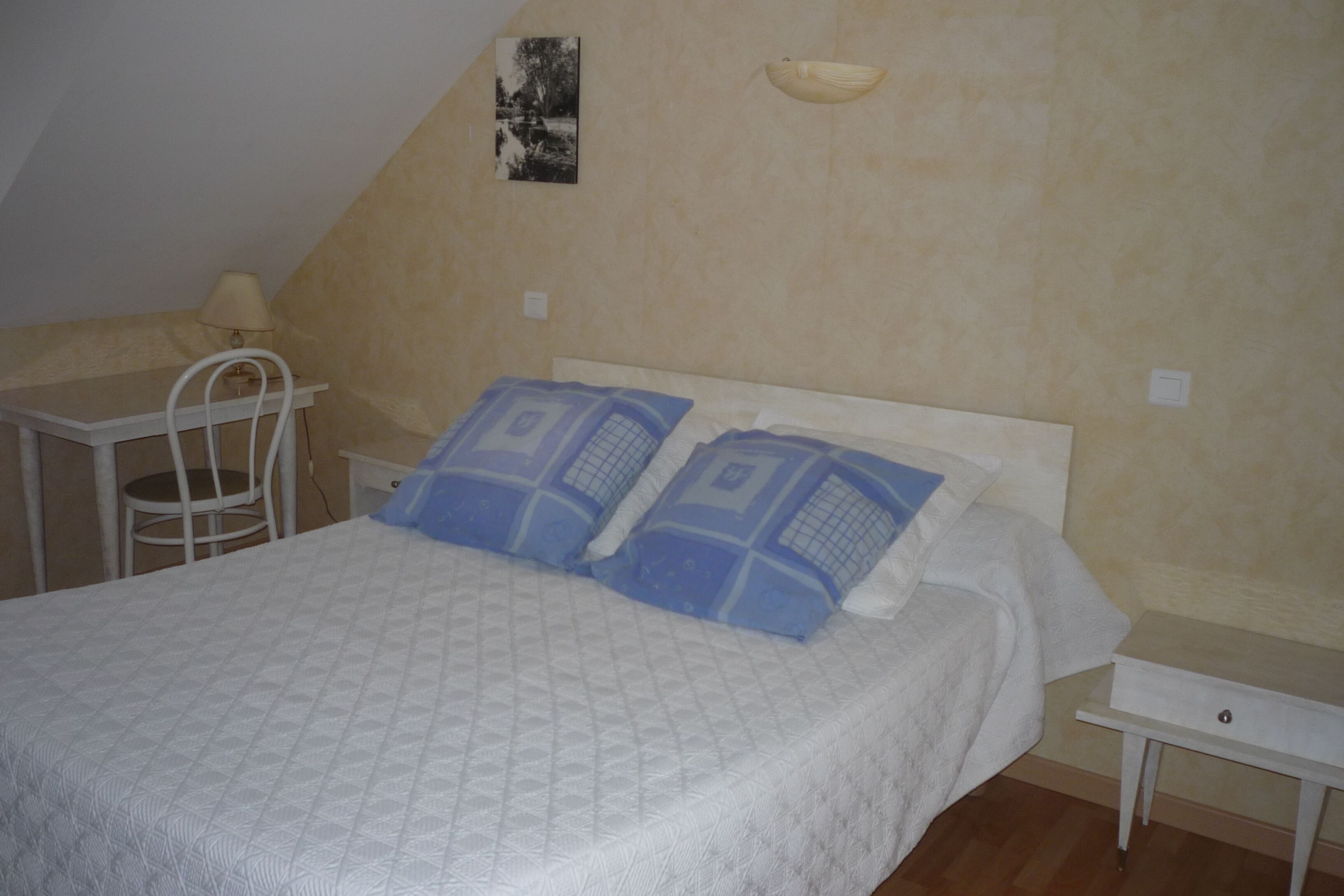 A bedroom with a bed, a nightstand, a chair, and a small table.