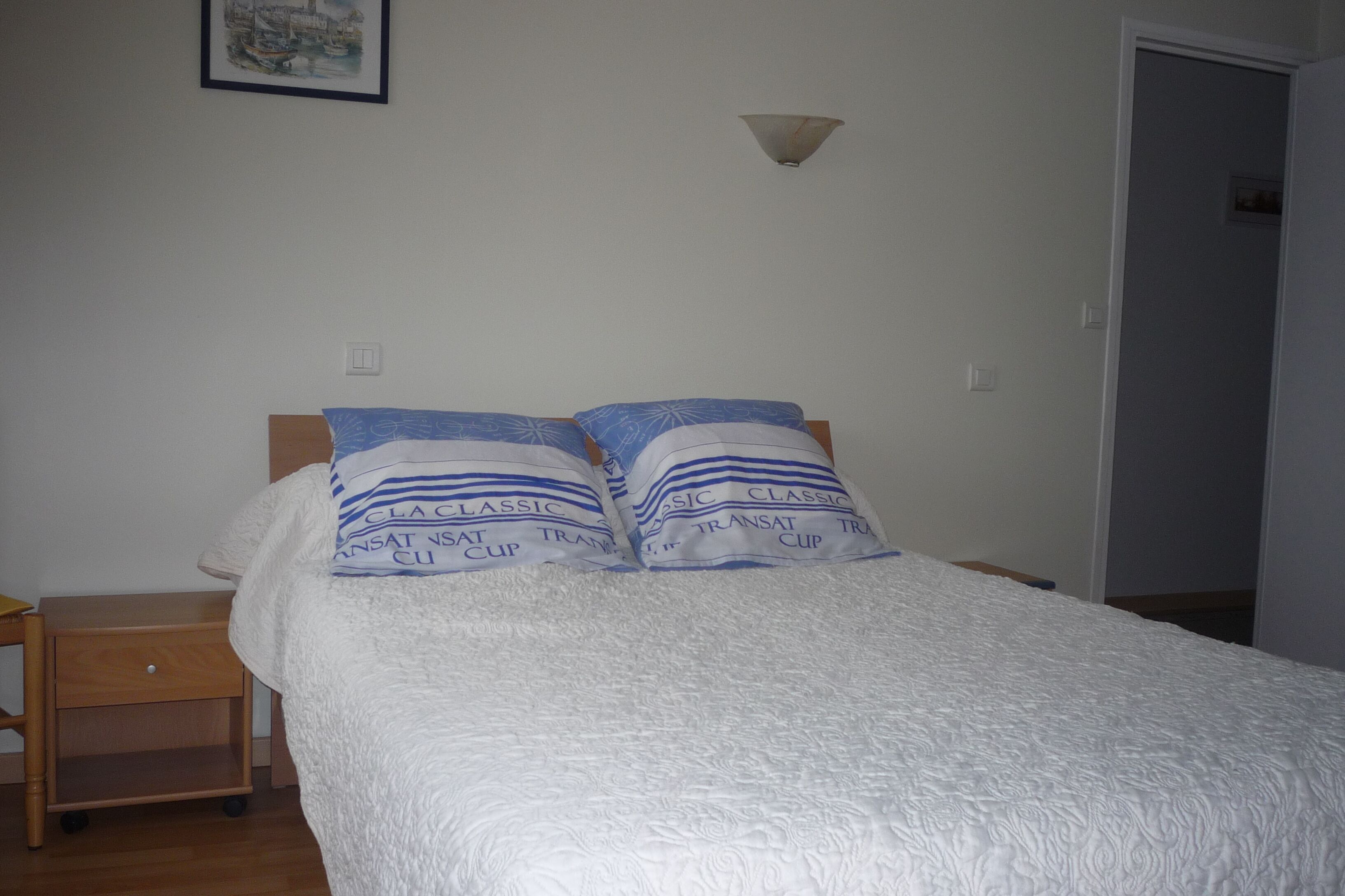 Un lit avec une couette blanche et deux oreillers à rayures bleues et avec du texte imprimé.