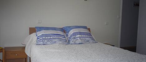 Un lit avec une couette blanche et deux oreillers à rayures bleues et avec du texte imprimé.
