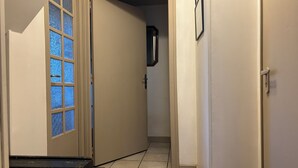Een gang met een deur naar een kamer, een klein vloerkleed en een aan de muur hangend fotolijstje.