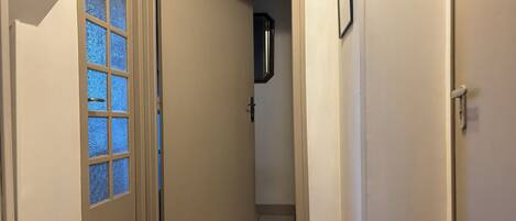A hallway with a door leading to a room, a small rug, and a wall-mounted picture frame.