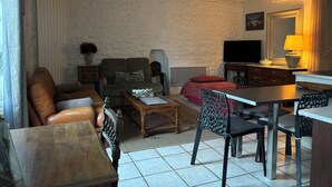 Een woonkamer met een bank, fauteuils, een salontafel, een televisie en een eethoek met stoelen en een tafel.