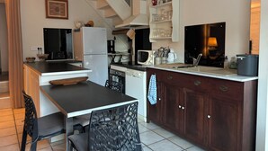 Een functionele keuken met een koelkast, magnetron, fornuis en spoelbak. Een eethoek met een tafel en stoelen is aanwezig.
