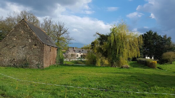 A stone building with a sloped roof, surrounded by a grassy field and trees.
