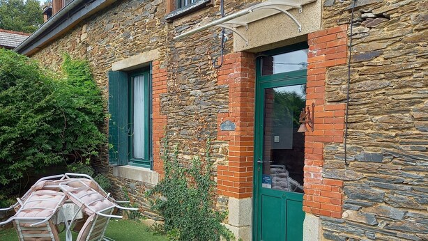 A stone house with a green door, a small garden with artificial grass, and a patio table and chairs.