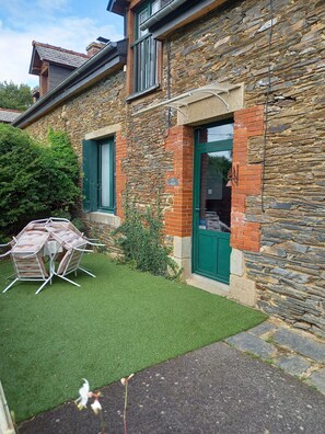 A stone house with a green door, a small garden with artificial grass, and a patio table and chairs.