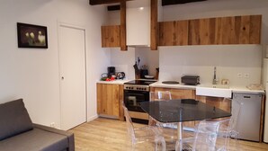 A modern kitchen with wooden cabinets, a stove, and a dishwasher. There is a dining table with clear chairs.