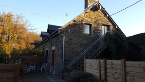 A stone house with a wooden staircase leading to the entrance, a small outdoor seating area with metal chairs, and a wooden fence.