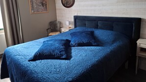 A bedroom with a large bed, a chair, a nightstand, and a wall with a picture frame.