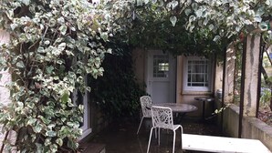 Een klein terras buiten met een tafel en stoelen, omringd door weelderige beplanting en een stenen muur.
