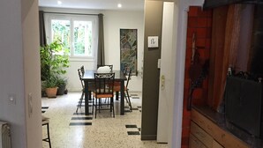 Een eetruimte met een grote tafel en stoelen, een raam met uitzicht op groen, en een betegelde vloer.