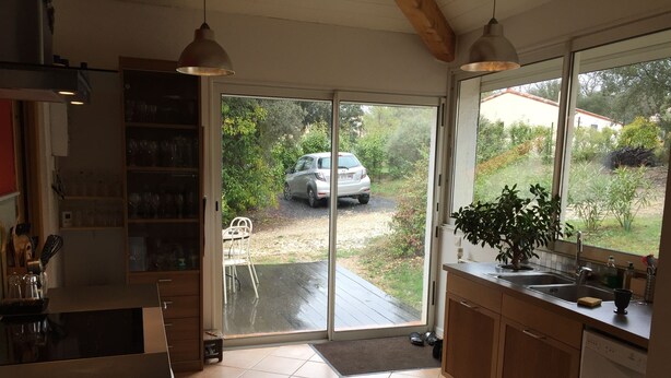 Een keuken met een groot raam, een eethoek met stoelen en een auto voor het gebouw.