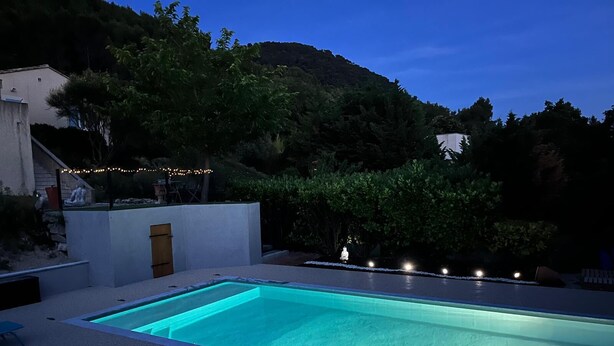 Una piscina rectangular con superficie de agua azul cristalina, rodeada por un muro blanco y una terraza de madera con sillas de descanso.