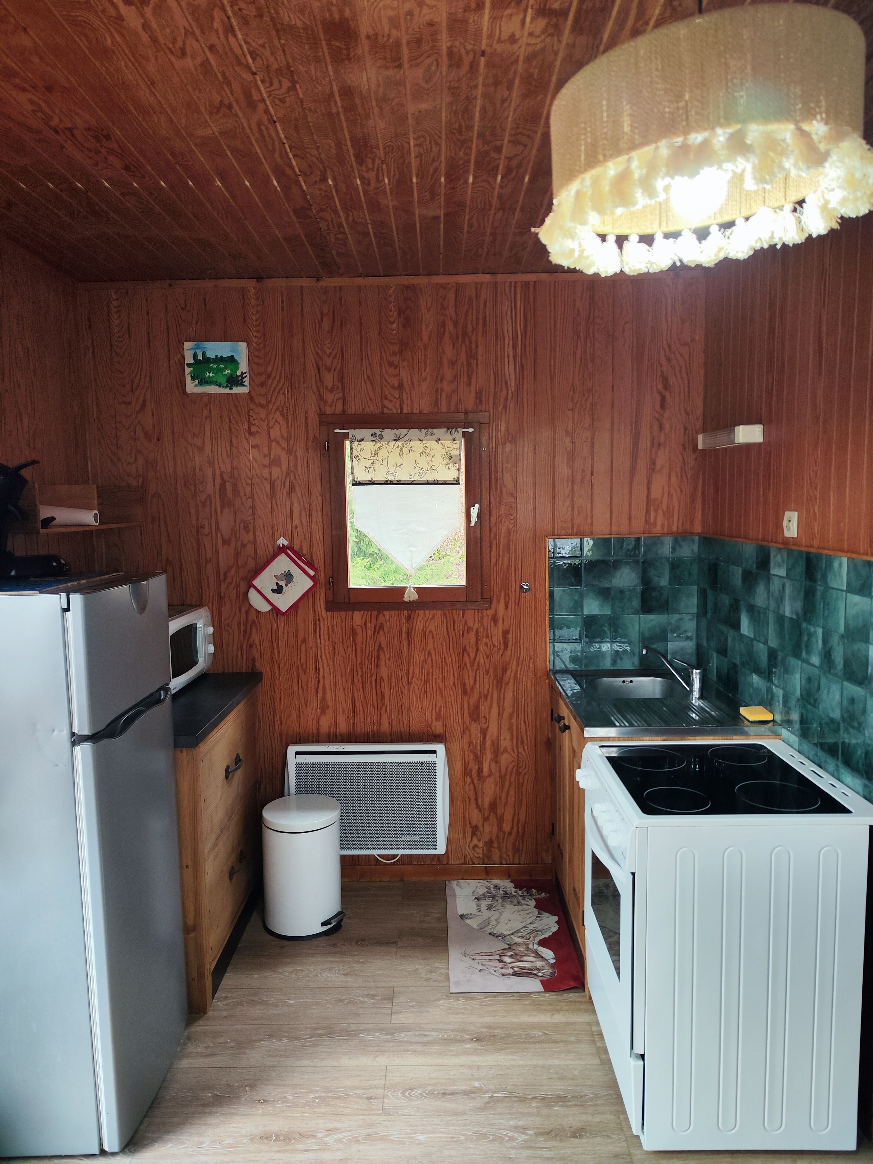 Una cocina compacta con paredes de madera, un ventanal pequeño, un microondas, un refrigerador, un lavamanos y una estufa.