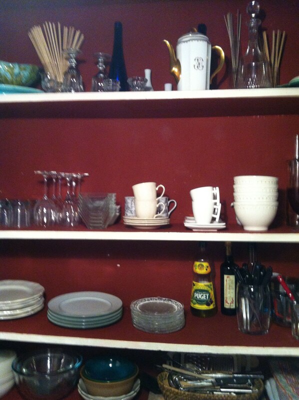 Una estantería de cocina con platos, vasos y utensilios.
