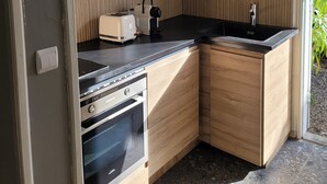 Una cocina compacta con armarios de madera, encimera negra, horno empotrado y lámpara colgante.