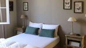 Un dormitorio con una cama doble, dos mesitas de noche, una lámpara colgante e impresiones botánicas enmarcadas en la pared.