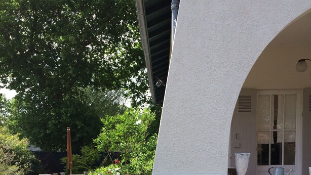 Un edificio blanco con un ventanal grande y una puerta. Hay un jardín con plantas y un camino de grava.