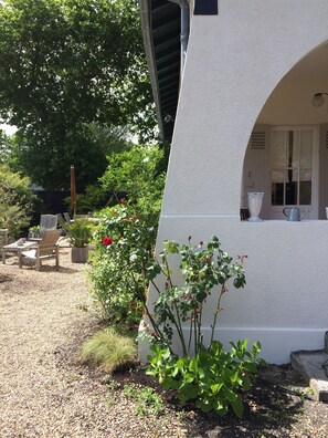 Un edificio blanco con un ventanal grande y una puerta. Hay un jardín con plantas y un camino de grava.