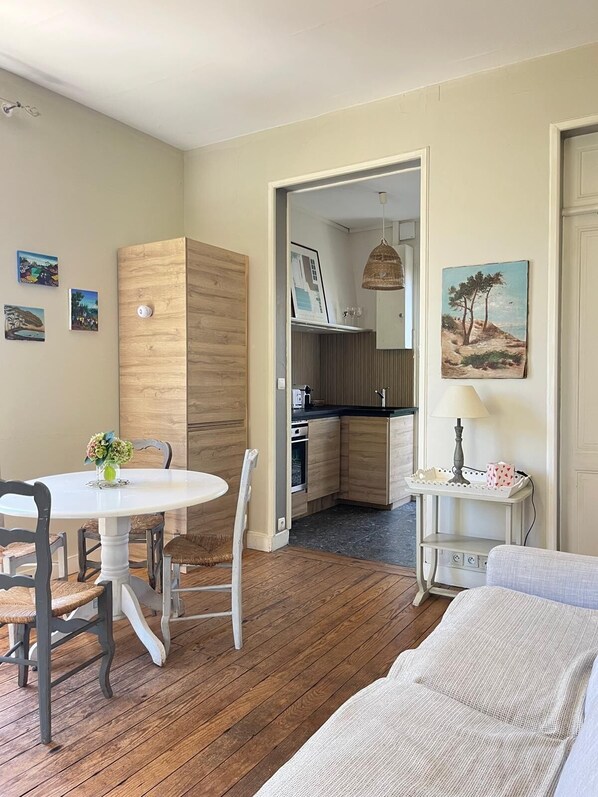 A modern kitchen with wooden cabinets, a dining area with a round table and chairs, and a painting on the wall.
