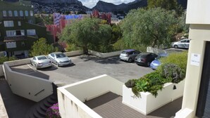 Un’area di parcheggio con diverse auto, circondata da edifici e vegetazione, con montagne sullo sfondo.