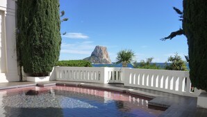 Una piscina con bordo curvo, circondata da una ringhiera bianca e con vista su una montagna rocciosa sullo sfondo.