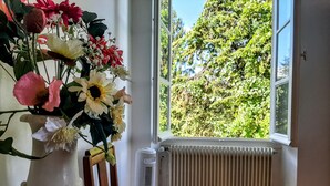 A room with a window, a radiator, and a vase with flowers on a table. - old farmhouse renovated (Aiguillon)
