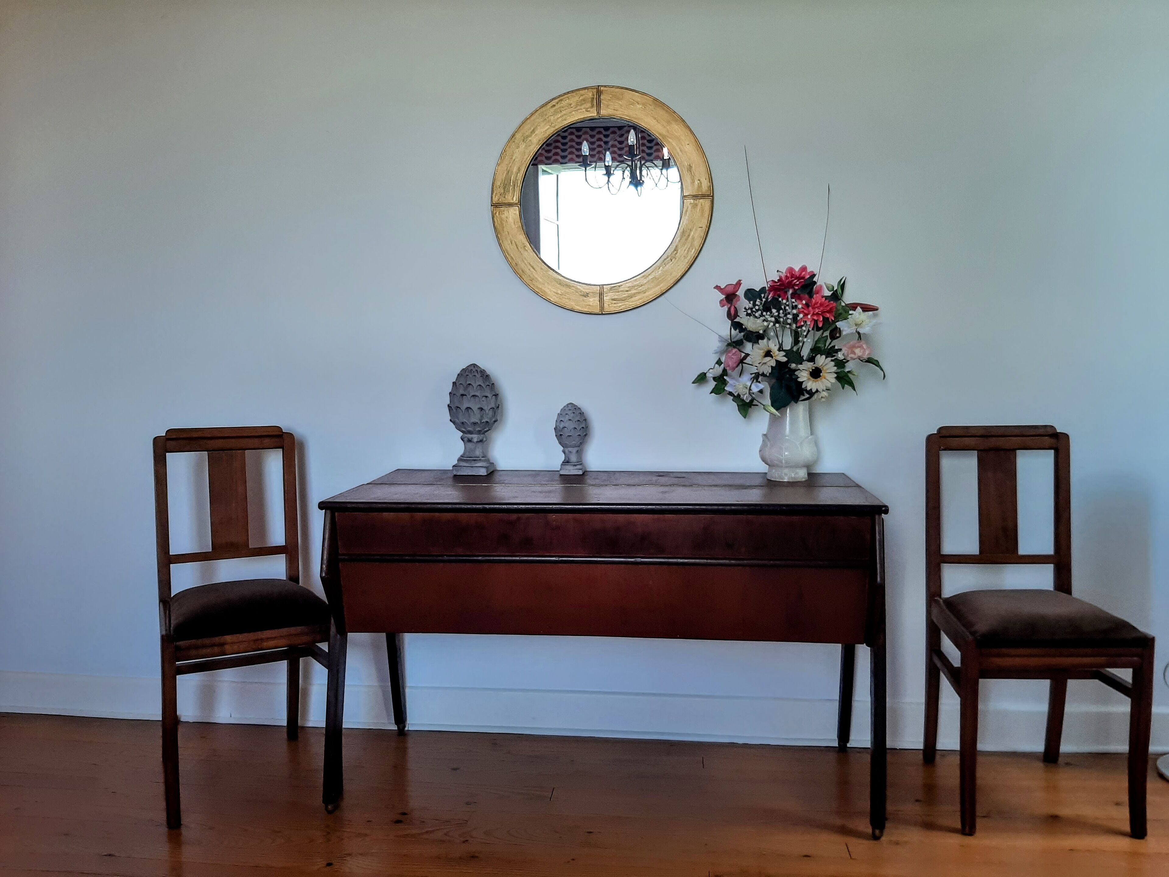 A wooden desk with two chairs, a mirror, and a vase with flowers.